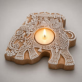 A carved wooden elephant-shaped block print tea light candle holder with intricate white patterns lit for Diwali decoration
