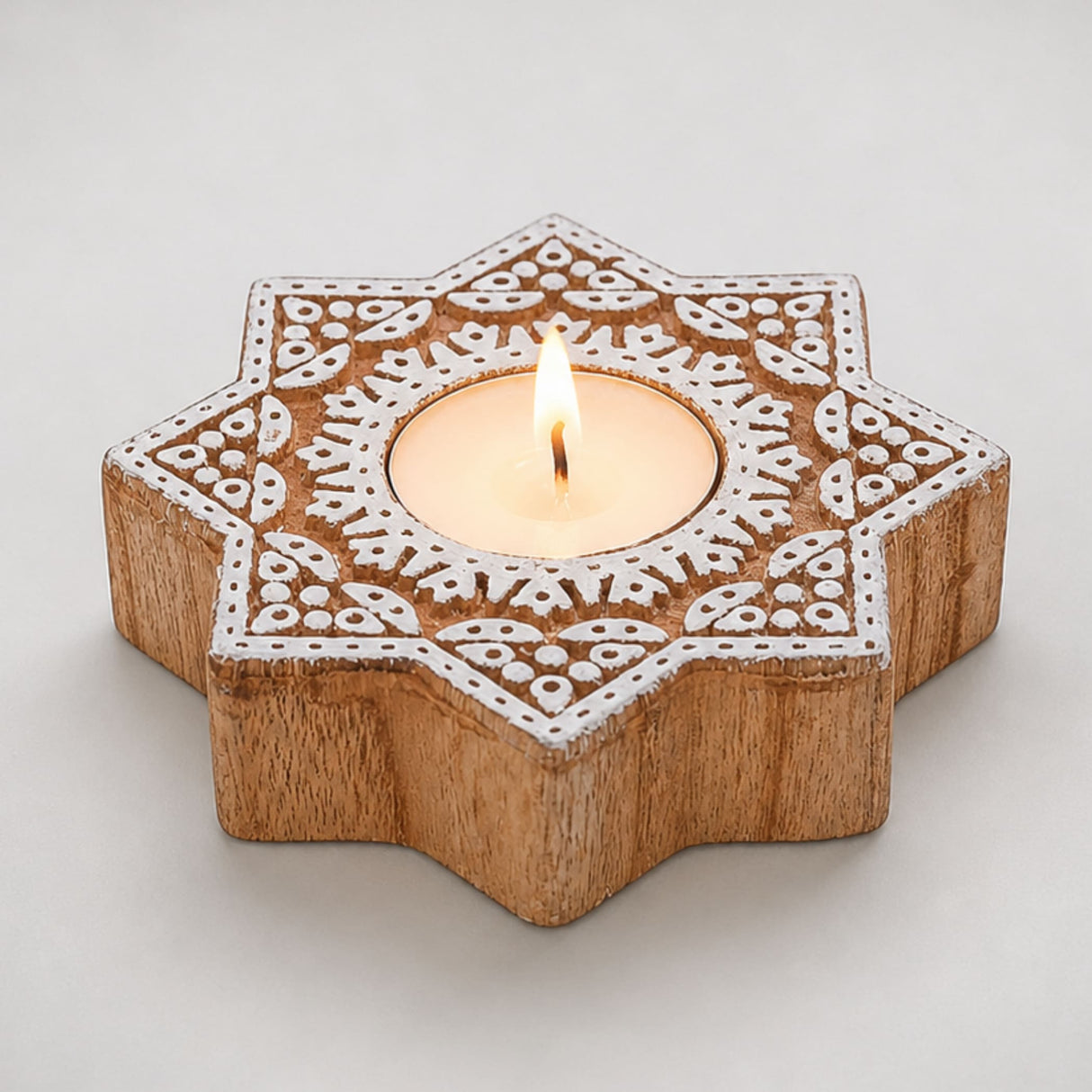 Wooden star-shaped block print tea light candle holder with white carved patterns holding a lit tlight for diwali decor