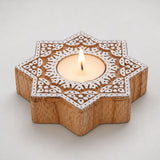 Wooden star-shaped block print tea light candle holder with white carved patterns holding a lit tlight for diwali decor