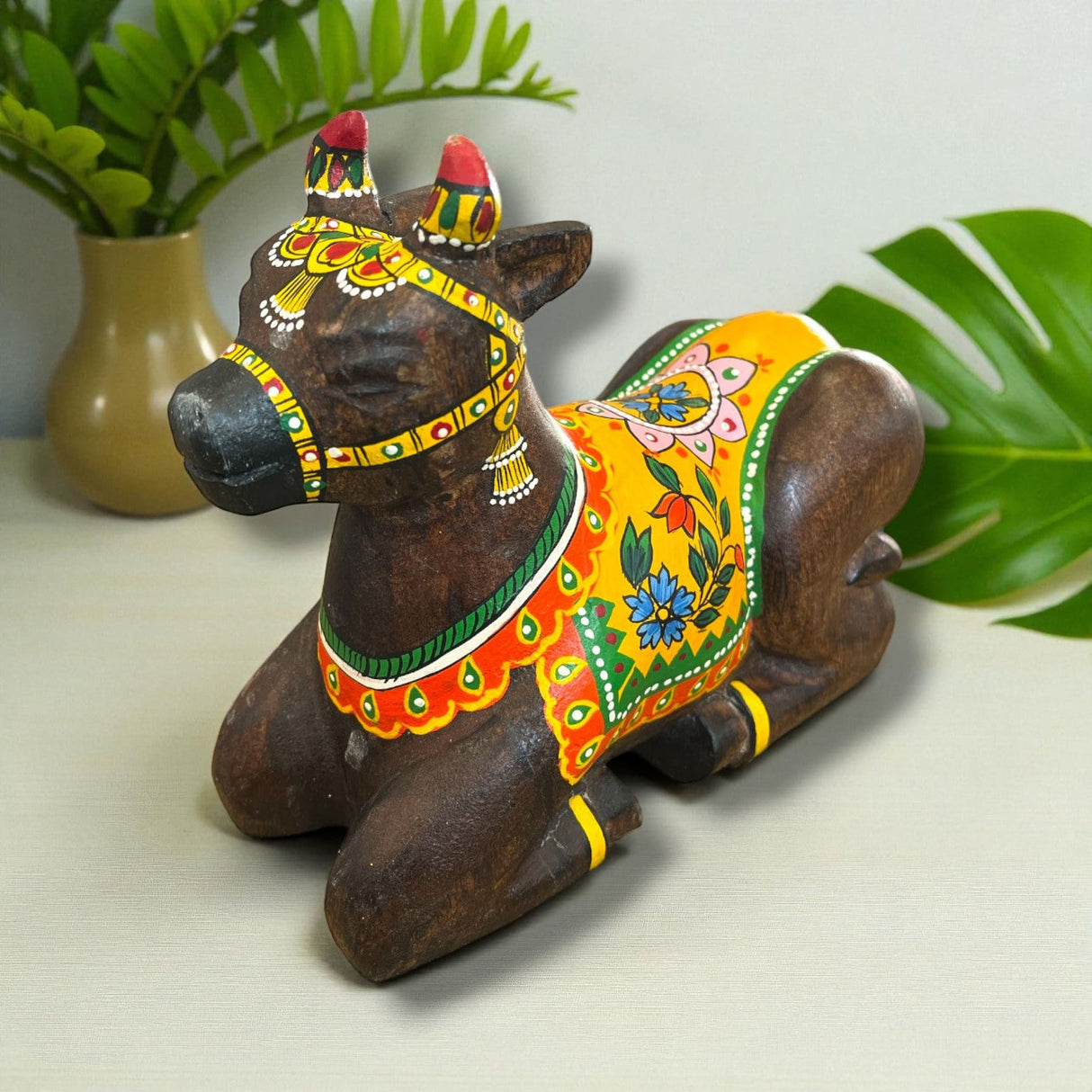 Handmade wooden Nandi cow idol with floral patterns and red headdress