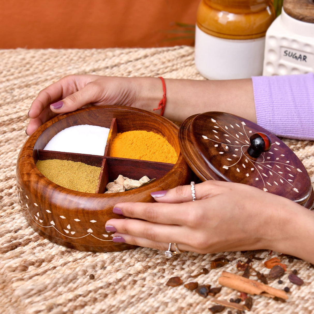Hand carved round wooden indian spice box with white inlay and four compartments holding turmeric sugar mustard and ginger