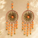 A pair of peach dreamcatcher earrings with gold frames pink trim and pom-poms in traditional Rajasthani style